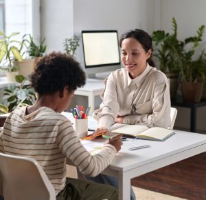 Portrait of smiling young woman as psychologist helping Black family in therapy session with young child drawing pictures
